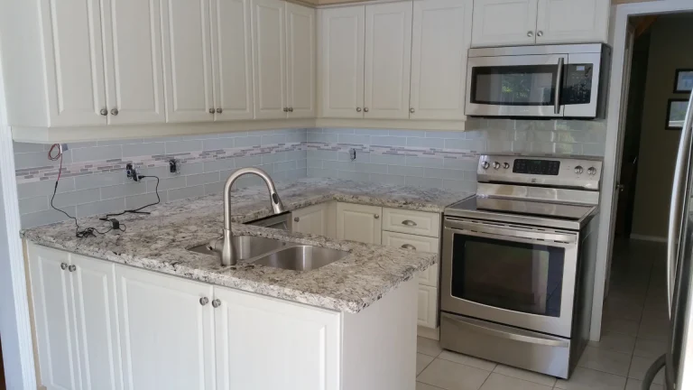 The transformed kitchen features white seamless doors, modern hardware, granite countertops, and a glass backsplash.